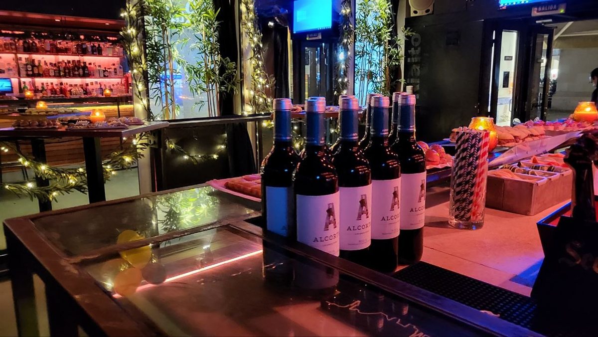Botellas de vino en la barra con lucecitas y plantas