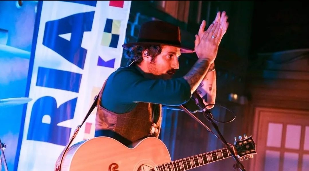 Concierto acústico en una fiesta de Rialto, con el panel de Rialto al fondo